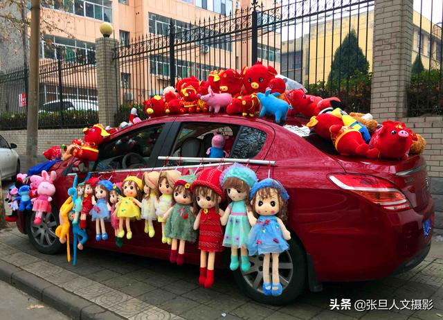 一名大学生开着汽车 装满中国红的布娃娃 说卖掉才是农民工的收入