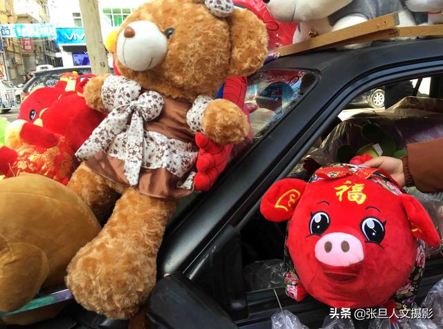 一名大学生开着汽车 装满中国红的布娃娃 说卖掉才是农民工的收入